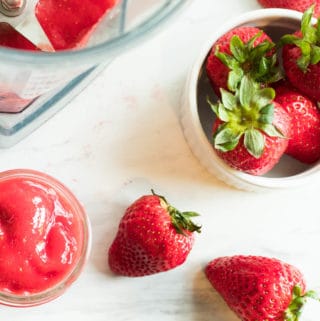 strawberries in a bowl with empty blender and small jar of strawberry puree