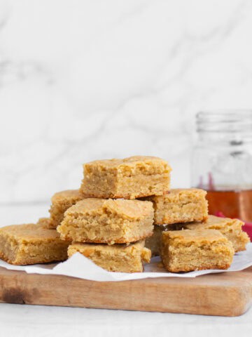stack of bourbon blondies on a tray with bourbon in background.