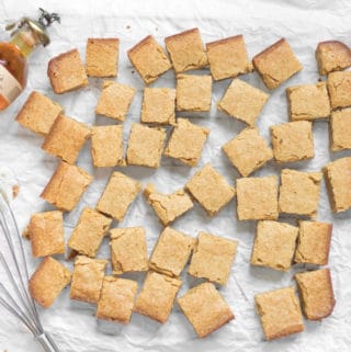 batch of boozy bourbon blondies scattered on parchment paper with a small bottle of blantons bourbon and a whisk