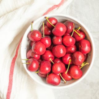 bowl of red cherries next to a white towel with a red stripe