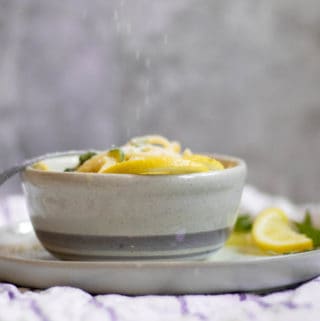 gray bowl with lemon garlic basil pasta. lemon and basil leaves used as garnish on plate