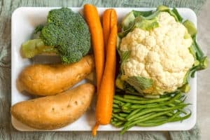 white tray with head of broccoli, head of cauliflower, carrots, green beans and sweet potatoes ready to make into baby food