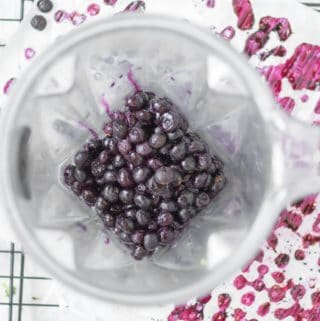 blueberries in a vitamix blender container with blueberry spotted parchment paper below