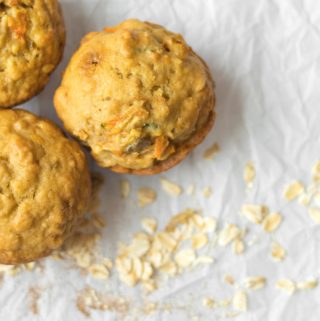 three apple cinnamon oatmeal breakfast muffins on parchment paper with rolled oats