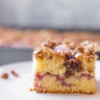 coffee cake with struesel on top and a strawberry jam swirl in the middle with a full pan of coffee cake out of focus in the background