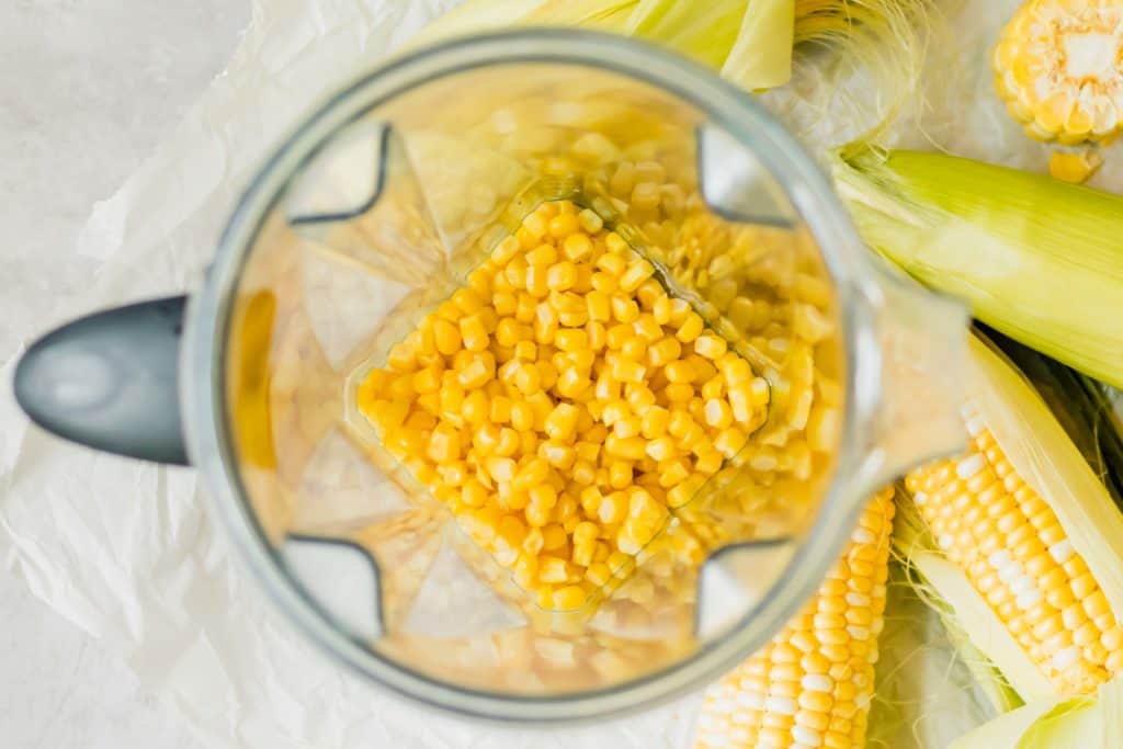 sweet corn kernels in a vitamix blender with whole ears of corn on the side
