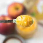 peach puree on a baby spoon held over a mason jar of puree and whole peaches