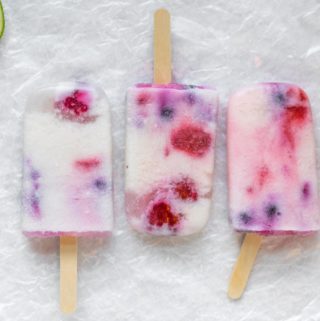 three red white and blue popsicles with wooden popsicle sticks and lime slices on the side