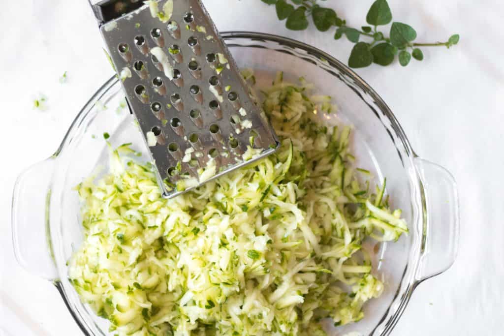 shredded zucchini in a glass bowl with a box grater