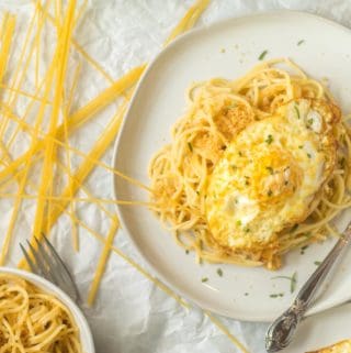 pasta pangrattato on a white plate with a fried egg on top with dried pasta on parchment paper