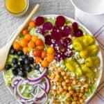 composed greek salad with piles of chickpeas, onions, tomatoes olives, beets and pepperoncinis on big serving dish with wooden spoon
