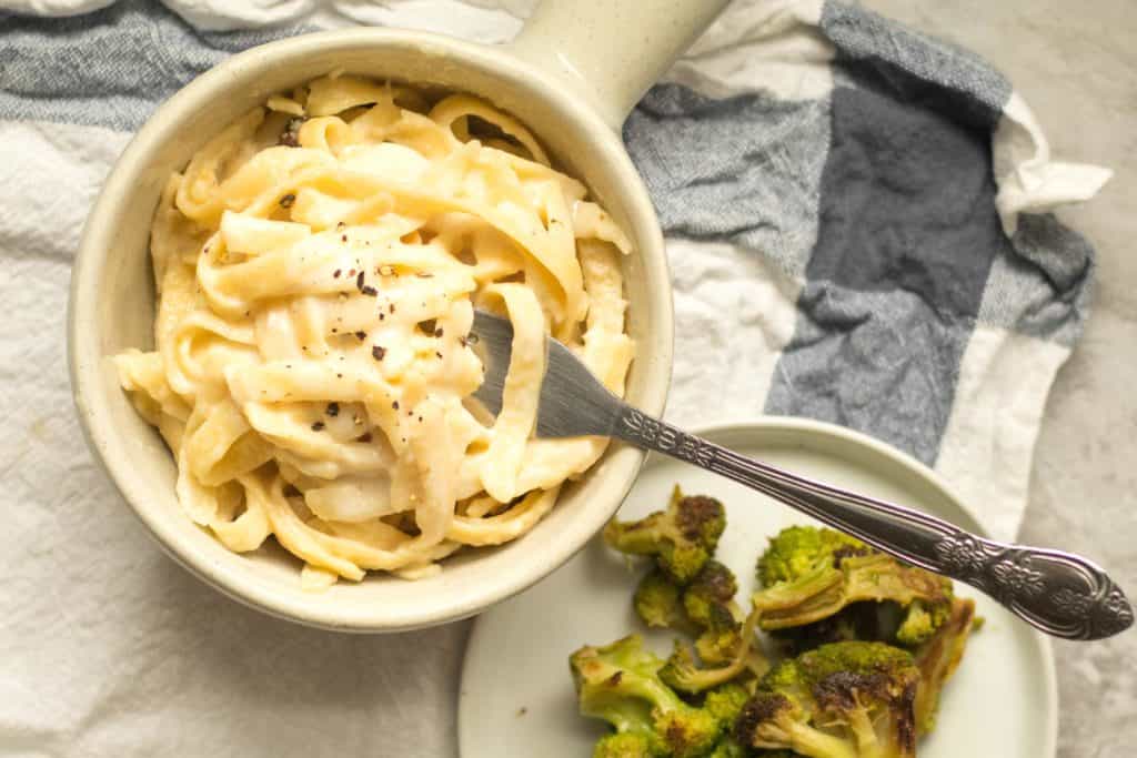simple fettuccine alfredo piled in a ceramic crock with broccoli on the side.