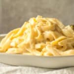 simple fettuccine alfredo piles high on a plate with broccoli in the background