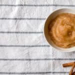 bowl of homemade applesauce with cinnamon sticks on a striped tablecloth