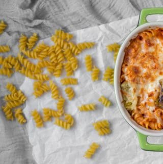 artichoke pasta bake in a green ceramic dish with dried pasta around it