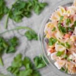 greek pasta salad in a glass bowl with parsley leaves all around