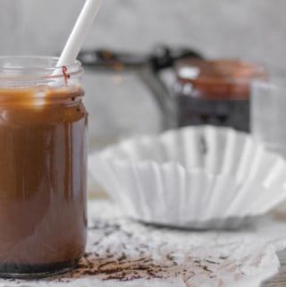 iced mocha in a mason jar with coffee filter, pot and chocolate sauce in the background