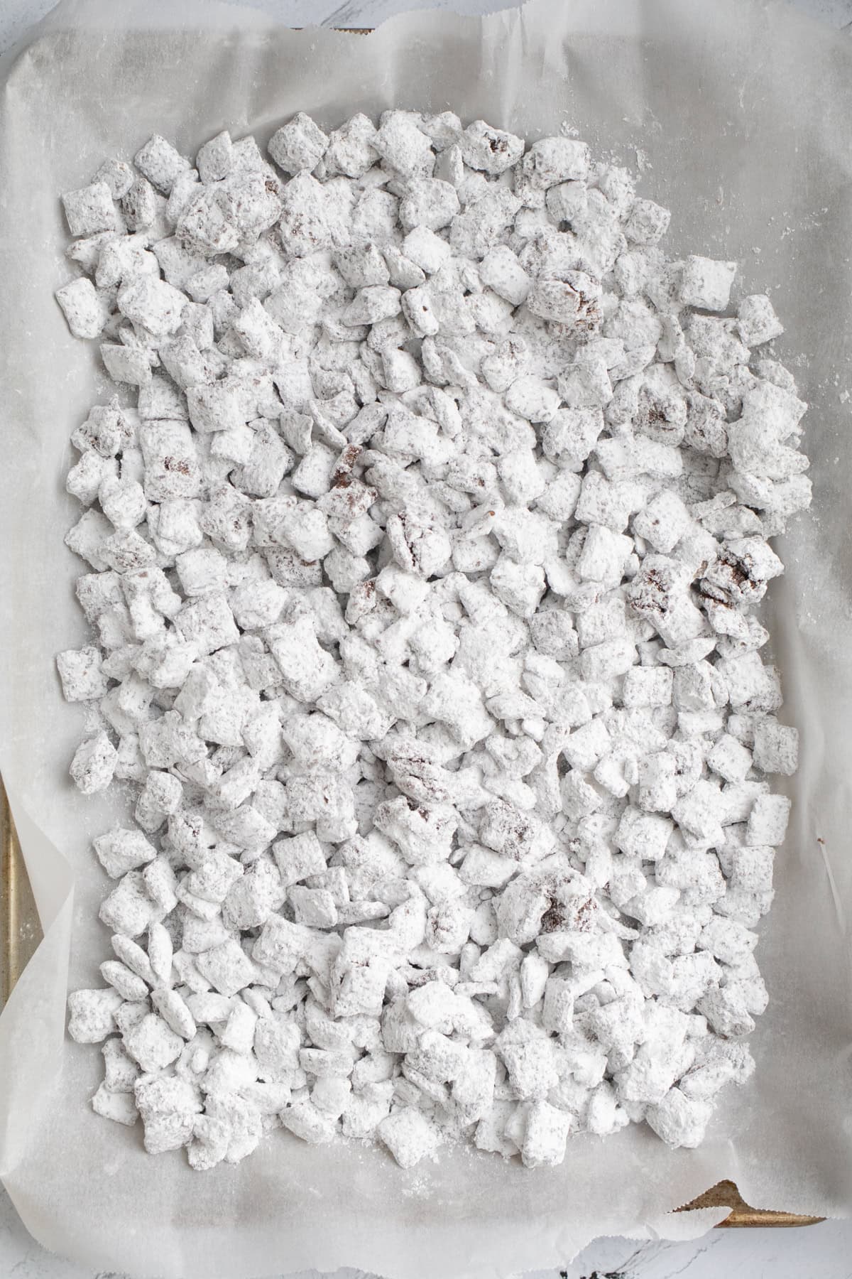 chocolate coated chex mix tossed with powdered sugar on a sheet tray.