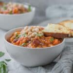 side view of bowl of minestrone soup with cheesy toast resting on top