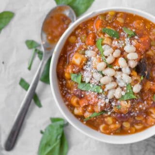 bowl of minestrone soup garnished with herbs, parmesan and white beans