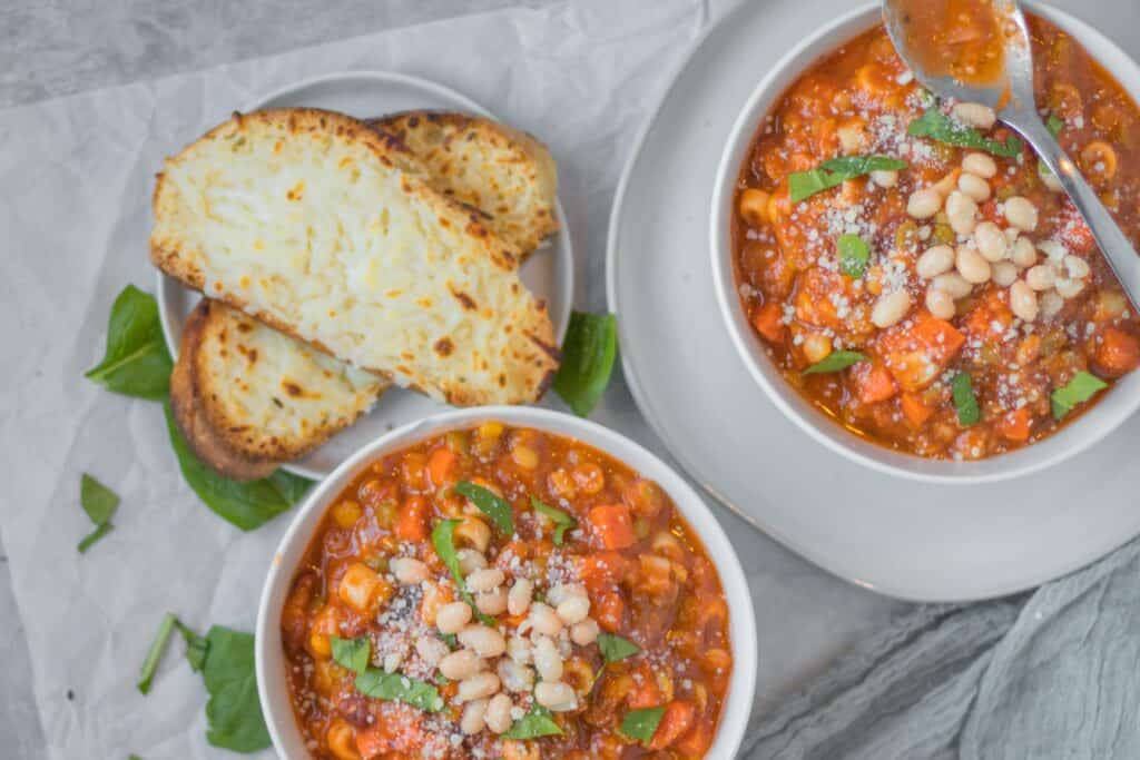 two bowls of minestrone soup with cheesy bread on the side