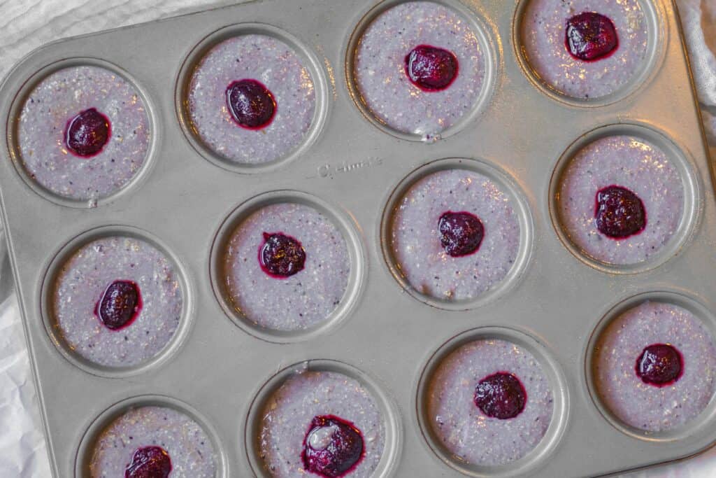 muffin batter in muffin tins with cherry pushed into the middle of each muffin