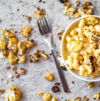 bowl of cauliflower mac 'n cheese with roasted cauliflower on parchment paper with a silver fork