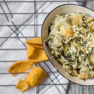 bowl of spinach artichoke dip with corn chips spread around