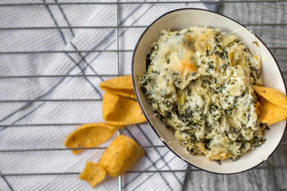 bowl of spinach artichoke dip with corn chips spread around