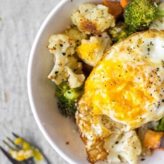 everything bagel seasoning over roasted veggies and a fried egg in a white bowl