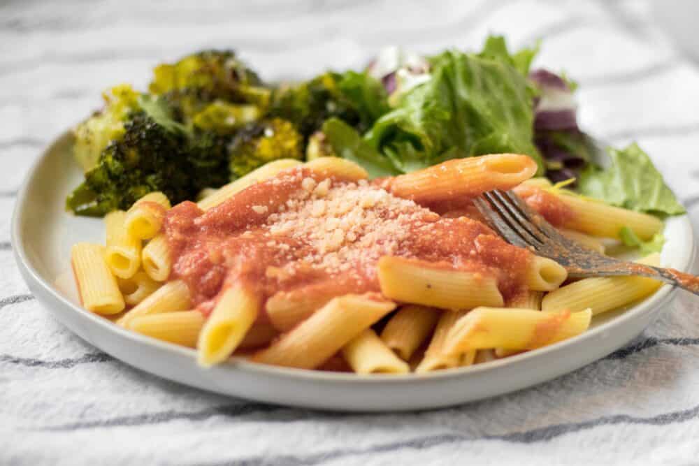 pink sauce pasta on a plate with salad and broccoli