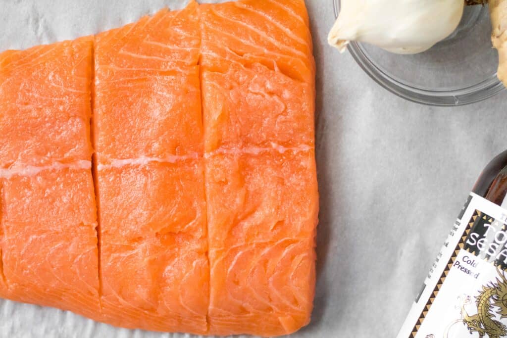 raw salmon scored into fillets with a jar of sesame oil to the side