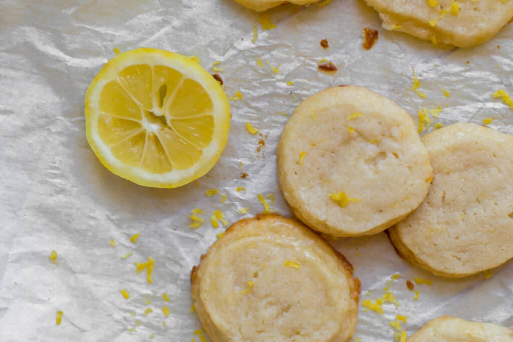 3 lemon shortbread cookies with a slice of lemon on parchment paper