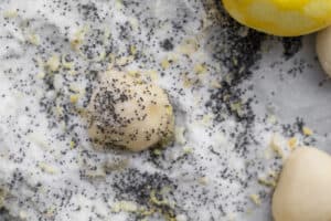 dough ball being rolled in lemon sugar and poppy seeds
