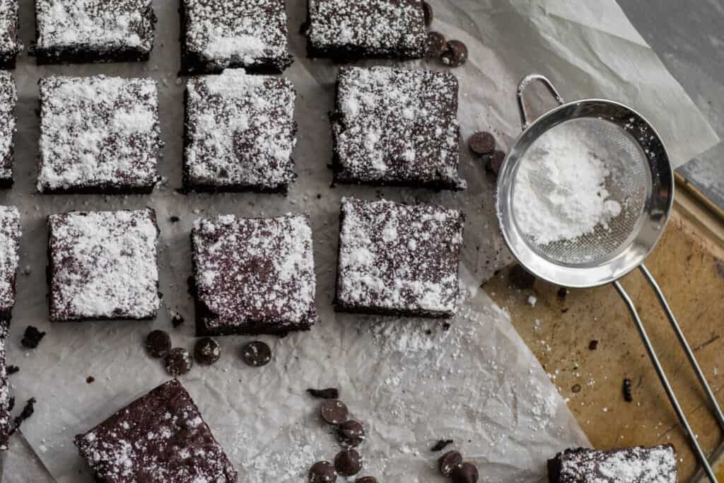 brownies on parchment paper with powder sugar in sifter