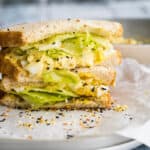 egg salad sandwich on a white plate with everything bagel seasoning around it