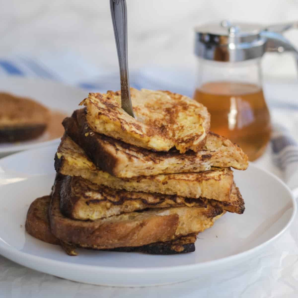 french toast piled on a plate with a syrup container in the background