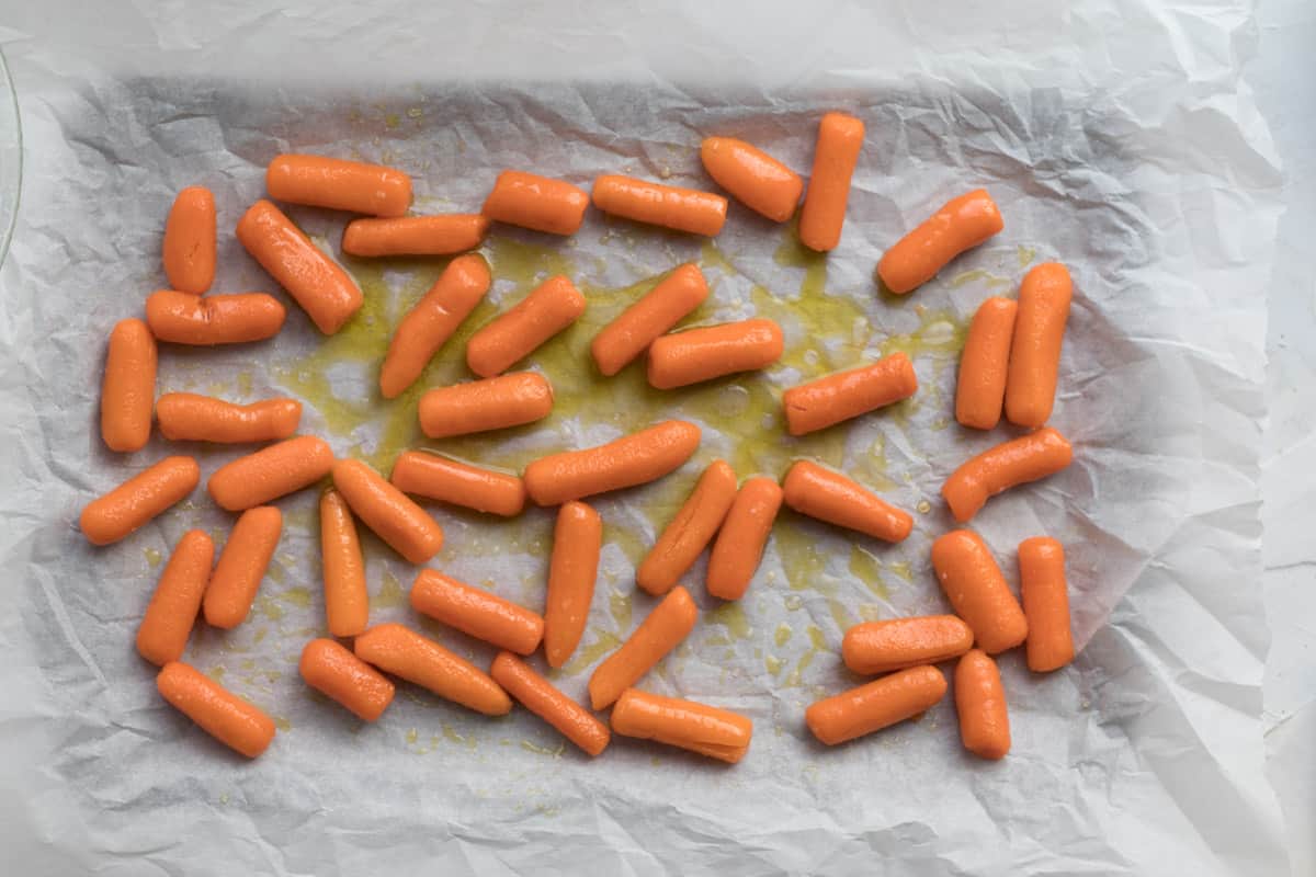 seasoned baby carrots on a baking tray covered in parchment paper