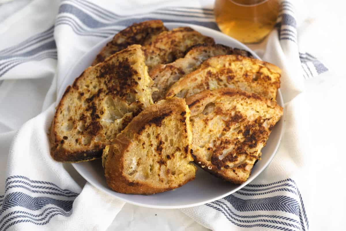 sourdough french toast piled high on a plate with syrup in the background