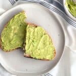 Avocado toast with flaky sea salt and cracked black pepper on a white plate