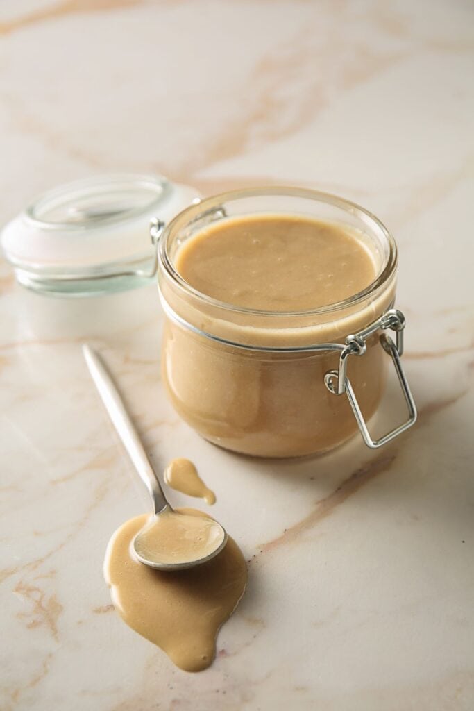 tahini in a jar with a spoon next to it.
