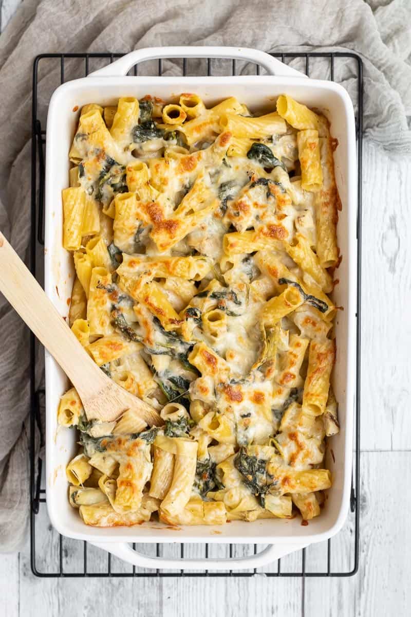 baked spinach artichoke pasta in a rectangle baking dish.