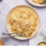 lemon and garlic pasta in a serving dish with serving spoon, garnished with lemon.