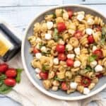 caprese pasta salad in a bowl with garnishes along side.