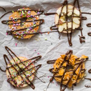 4 apple slices on parchment paper decorated as donuts