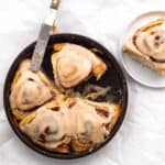 cinnamon rolls with icing in a round pan with small spatula