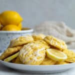 lemon cake mix cookies on a plate with a bowl of lemons behind