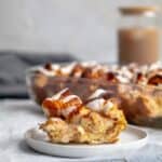 piece of cinnamon roll casserole on a white plate with the baking dish behind