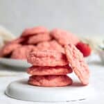 four strawberry cake mix cookies stacked on a white plate.
