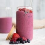 mixed berry smoothie in a glass cup with the lid next to it